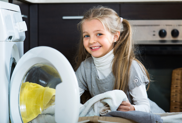 Happy cute little girl with long hair doing laundry in home interior
